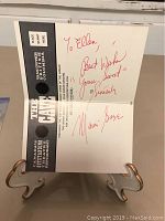Brochure open on display stand showing red autograph across inner panels