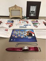 Overview of all items including coin set, Guess watch with red strap, workout CDs, two frames, and motorcycle clock.