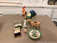 Various ceramic and decorative items including a cow creamer, rooster figurine, pie bird, jewelry boxes, and a decorative dish shown on a table.