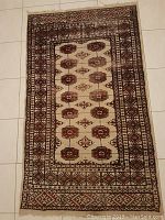 Full view of hand knotted rug laid out flat on tiled floor. Shows entire design with geometric medallions and border.