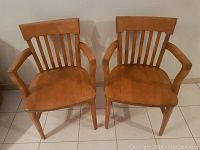 Pair of maple wood chairs with armrests and vertical back slats, showing front view.