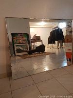 Full view of large rectangular mirror leaning against wall showing etched floral corners and beveled edge.