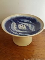 Side view of large pedestal comport, showing blue and cream glaze artistic pattern inside with pedestal base, placed on a wooden surface.