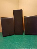 Photo of the three speakers with black cloth covers on, two bookshelf speakers and one tall speaker in the middle.