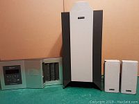 Full view of Nakamichi SoundSpace 8 stereo system including main unit, large center speaker, and two smaller speakers on green surface against pink background.