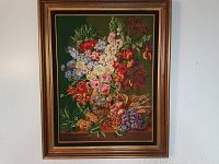 Full view of vintage floral needlepoint artwork framed with a gold-tone frame on a white background.