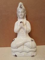 Front view of white porcelain Buddha statue seated with hands in prayer position showing crackle glaze and brown patina marks.