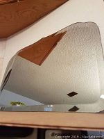 Large rectangular antique beveled mirror with patterned hand cut edges, placed on wooden surface showing reflection of ceiling and room.