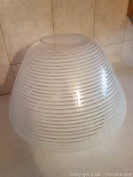 Angled photo showing the overall rounded tapered shape of the glass shade with white horizontal stripes.