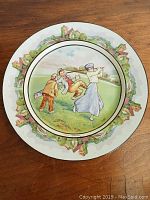 Full view of round plate showing colorful golf scene with three early 1900s characters outdoors, village scenery around rim