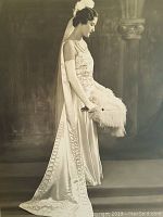 Close-up of the profile portrait of a young woman in an elaborate Art Deco gown, gloves, and feathered fan.