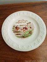 Full view of the antique plate showing embossed alphabet around the rim and central illustration of children playing.