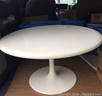 Full view of white round low coffee table with single pedestal metal base showing overall structure.