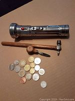 Photo showing flashlight, small hammer, small carving tool, and scattered coins on surface.