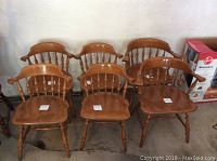 Full view of six wooden maple chairs, four side chairs, and two armchairs in a row against wall.