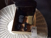 Photo of optics lot box with Crystar opera glasses, Bushnell pouch, and additional items inside a cardboard box