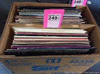 Box containing 26 vinyl records of mostly 70s and 80s rock music, showing some visible album covers including 'The Stranger' by Billy Joel.