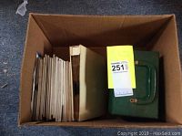 Box showing large quantity of 45 rpm vinyl records in cardboard sleeves along with a green metal carrying case inside the box.