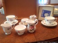 Photo showing assorted tea cups, saucers, and creamer pitchers with floral designs and gold trim.