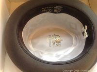 View of the inside of the hat showing cream satin lining with gold Stetson logo, including size information and interior band.
