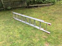 Full view of the 13 foot aluminum ladder placed horizontally on grass.
