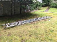 Extended aluminum ladder lying on grass, showing two sliding sections and green rung locks