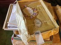 Overview of linens in box including a yellow R.H. Stewart linen tablecloth in original package, cream and beige folded linens, and crochet doily.