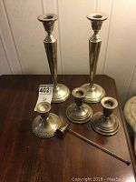 Six silver candle holders and a candle snuffer arranged on a wood surface showing overall set, sizes and shape.