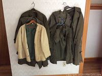 Five vintage military jackets hanging on a wall, varying in style and color with one beige fleece liner