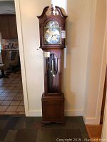 Front view of full grandfather clock showing bonnet top, dial and base