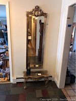 Full view of the ornate gold wall mirror mounted on the wall above the matching table.