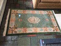 Green oriental style area rug laid flat on floor showing full rug pattern and condition