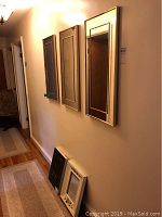 View of three matching large rectangular mirrors with gold trim and antiqued glass on wall alongside two smaller hand painted wood frame mirrors leaning below