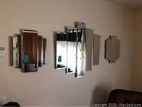 Three-piece beveled mirrored wall clock set mounted on a beige wall, including center clock and two matching side mirrors.