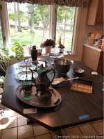 Silver plated coffee serving set on a table near window with tray, creamer, sugar bowl, and additional silver pieces and bowls visible in daylight.