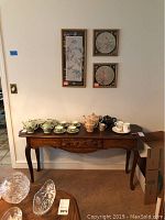 Photo showing wooden side table against wall with assorted tea sets arranged on top and three framed wall art pieces hanging above.