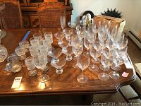 Photo showing a large collection of Gorham cut glass stemware on a wooden dining table including various wine glasses, dessert cups, and decanters.