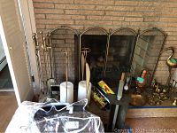 Fireplace tool set on stand along with two large white candles and brass fire screen positioned behind the fireplace hearth.