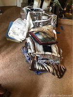 Stack of folded blankets, throws, and pillow in clear plastic bag next to some tablecloths on carpeted floor