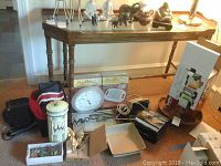 Wide view of all lot contents showing box of Bella Rocket Blender, micro hot plates, clock, hand mixer, grilling machine pan, decorative items, and two ceramic trivets.