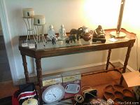 Full view of the sofa table placed against a wall showing wooden frame and glass top with decorative items on top.