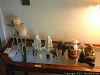 Wide shot of the collected Buddha, elephant figurines, ceramic vases, and candle holders displayed on a wooden table with glass top under warm lighting.