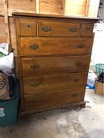Front view of wooden dresser showing seven drawers and metal handles with visible wear on surface.