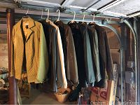 Seven assorted medium weight jackets hanging on a rack showing different colors and materials including leathers and fabrics.