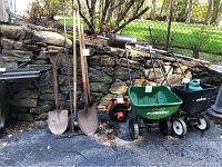 View showing three shovels, metal rake, two push spreaders, watering can and Echo leaf blower.