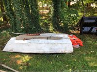 Wooden rowboat with two wooden oars, four orange life jackets, nautical American flag, and anchor laid on grass.