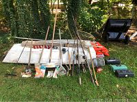 Image showing full assortment of fishing poles, nets, wire trap, clam digger, orange life jackets, and three tackle boxes outdoors on grass.