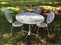 Full view of white painted wrought iron patio table with four mesh-design chairs on grass outdoors.
