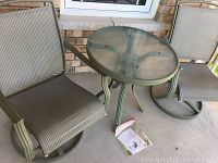 Wide view of both assembled swivel chairs and round glass-top table on patio