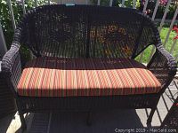 Front view of synthetic wicker love seat with striped cushion on deck